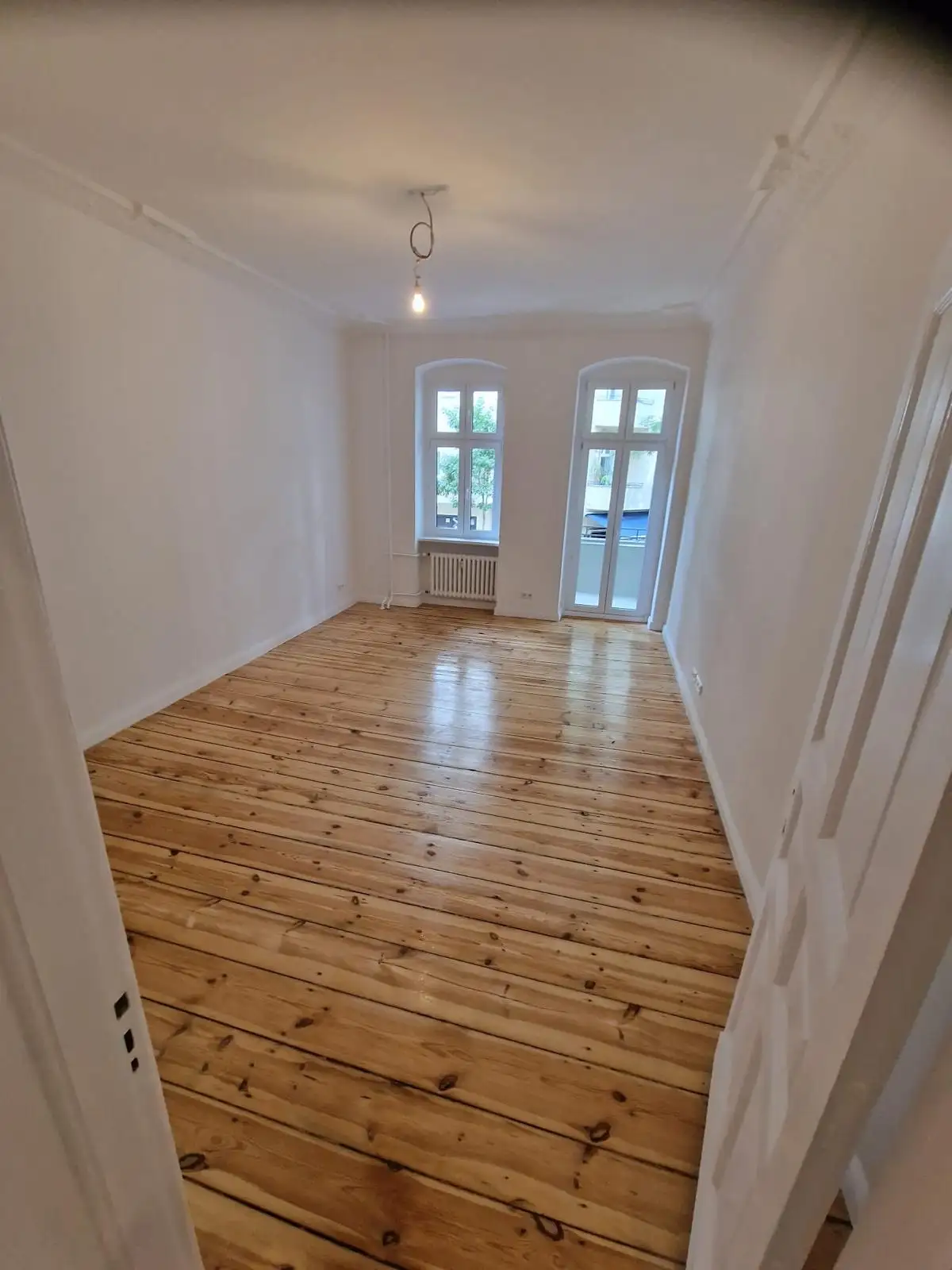 Zimmer mit Balkontür nach der Sanierung – helle Wände und geölte Dielen